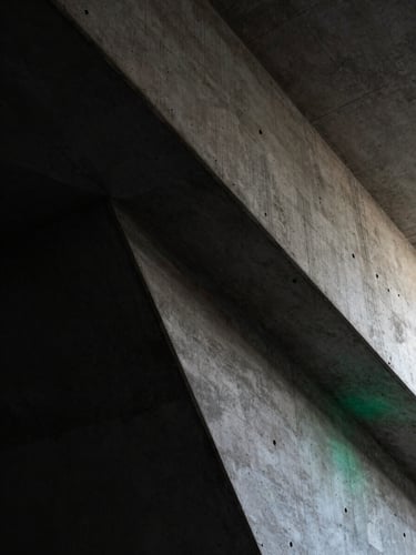Extreme close-up of high-contrast architectural concrete angles in low-key lighting, deep charcoal shadows, subtle emerald ambient light leak.