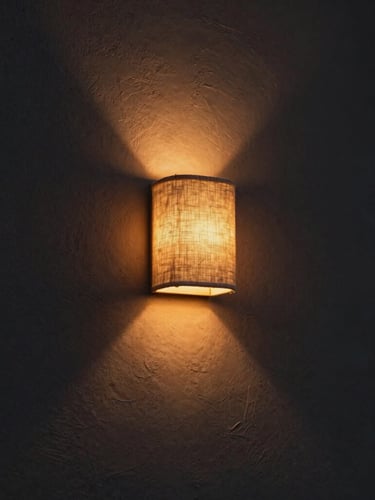 A tight architectural crop of a raw linen wall sconce casting a warm amber glow onto a dark textured plaster wall at twilight, 35mm lens, moody low-key lighting.