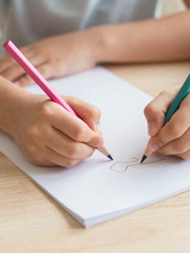 Close-up of children's hands writing with colorful wooden pencils on clean paper, soft natural daylight, warm sand tones, shallow depth of field