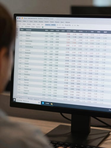 Close-up over-the-shoulder view of a monitor displaying a financial report table with columns of figures and row labels, cool ambient office lighting, sharp screen text in focus, keyboard partially visible at bottom edge