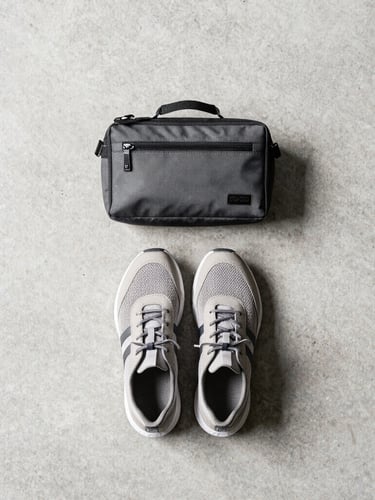 Overhead knolling flat-lay of technical travel accessories, a pair of lightweight shoes, and a compact tech pouch on a concrete background