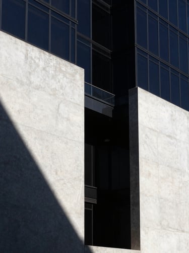 Crisp, high-contrast sunlight on a modern concrete and glass facade in Mexico City, sharp architectural shadows, deep navy tones, wide-angle lens, editorial style