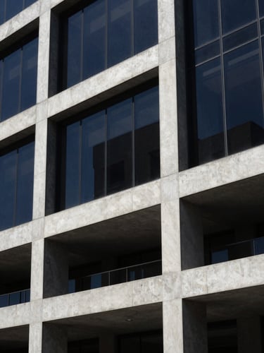 A sharp close-up architectural shot of a modern concrete and glass building facade in Mexico City, dramatic afternoon sunlight casting sharp geometric shadows, deep navy tones.