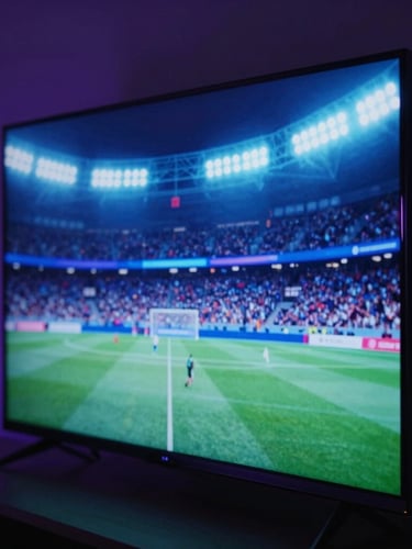 Macro close-up of a sleek smart TV screen displaying a high-action football match, glowing neon blue stadium lights reflecting off the bezel, moody dark room, 35mm