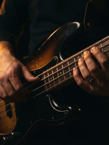 Moody close-up of hands playing a bass guitar, warm amber rim lighting highlighting the strings and fretboard, dark background, 50mm lens