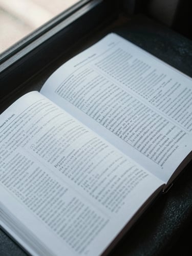 Close overhead shot of an open driver's guidebook with dense reference text visible on both pages, a printed test answer sheet overlapping one corner, cool daylight from a window off-frame left, no hands, no people