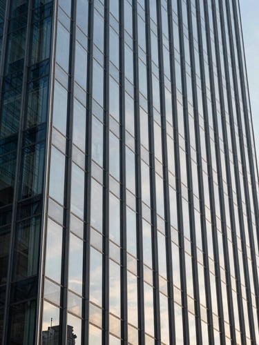 Crisp, vertical perspective of a modern glass and steel skyscraper facade reflecting a clear morning sky, emphasizing structural precision and scale.