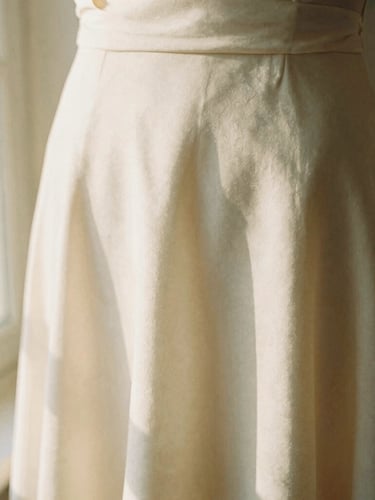 Close-up of a warm ivory silk dress catching soft window sunlight, showing the delicate drape and texture of the fabric, shallow depth of field, 35mm film