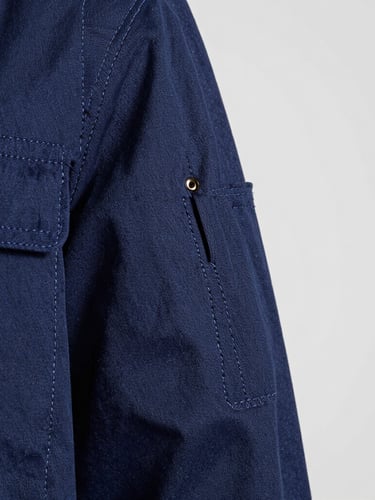 Extreme close-up of heavy-duty double stitching on a navy blue industrial work jacket, bright studio lighting highlighting the thread texture and stitch density, clean slate gray background.