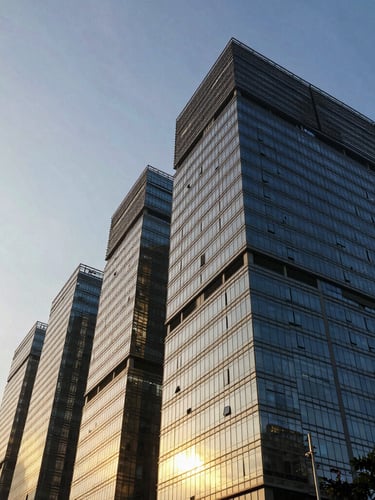 Low-angle dramatic golden hour shot of modern glass skyscrapers in Thane, light reflecting off concrete facades, negative space on the left