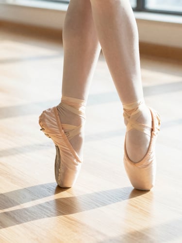 Close-up of laced pink ballet slippers and modern dance shoes on a sun-drenched light oak studio floor, bright high-key daylight, 35mm