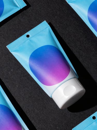 Tight macro top-down flat lay of high-fidelity physical cosmetic packaging mockups on a matte black surface, dramatic studio lighting with hard shadows and electric blue color-gel accents.