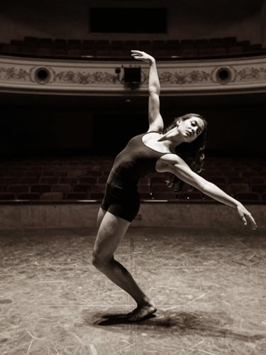 Elegant editorial dance photography of Victoria Holanda in a sharp physical extension, dramatic side-lit empty theater, high-contrast monochrome with warm clay undertones, 35mm
