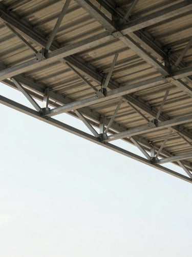 Wide panoramic 21:9 frame of a commercial building's exposed steel roof trusses, bright natural lighting, sharp architectural lines, expansive negative space on the left.