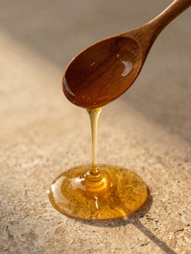 Overhead warm shot of organic honey dripping from a wooden spoon over a textured stone surface, soft golden hour side-lighting highlighting natural viscosity
