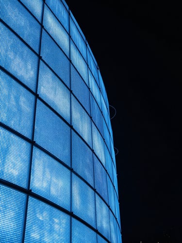 Extreme close-up portrait of a curved flexible LED panel installation at night, electric blue light tracing the arc of the curved screen surface, panel seams and bezels sharply detailed, deep black background, no people, technical precision in focus