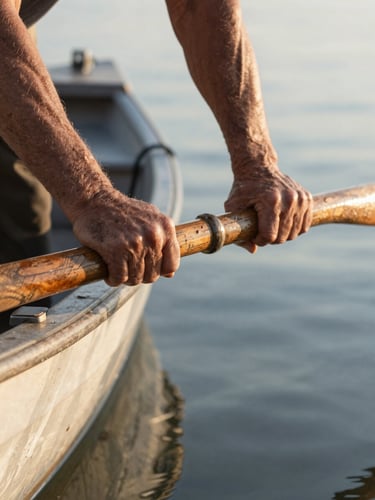 Close environmental portrait, a pair of weathered hands gripping the worn wooden oar of a fishing boat, natural early-morning sidelight from the left, water visible below out of focus, worn fibres of the wood grain sharp in foreground, framing is tight on the hands with the boat's prow extending into the right edge