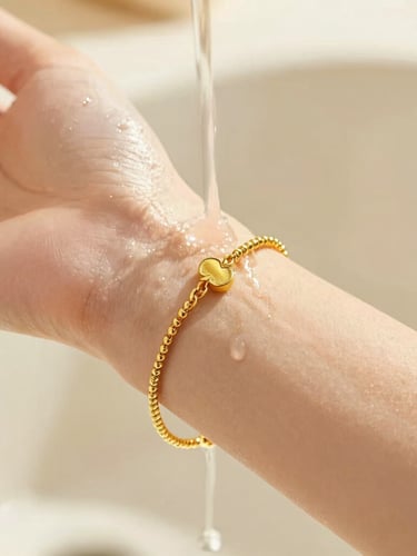 Extreme close-up of a delicate gold bracelet on a woman's wrist under running water, sun-drenched warm lighting, shallow depth of field, highlighting the metallic luster.