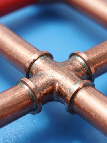 Macro shot of clean copper pipework with soldered joints, bright daylight, sharp focus on technical details, professional blue and red tones, 35mm