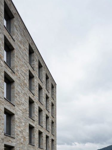 Wide environmental shot of a Zug office building exterior at midday, stone facade and clean architectural lines to the left third, overcast Swiss sky occupying generous upper space, no people visible