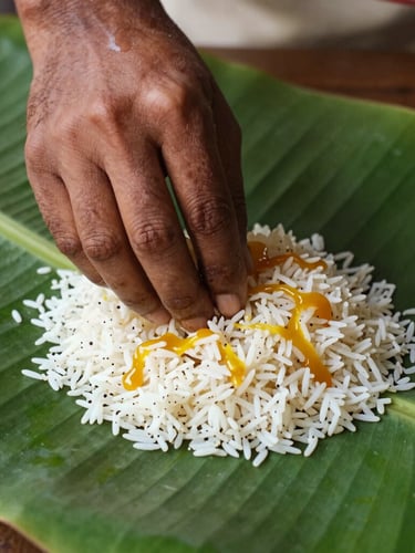 Vibrant close-up portrait of a guest's hand mixing rice with golden paruppu and ghee on a glossy banana leaf, warm natural light.