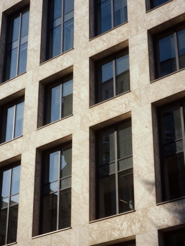 Architectural close-up of a modern limestone office building facade, sharp diagonal shadows, warm sunlight, editorial corporate photography