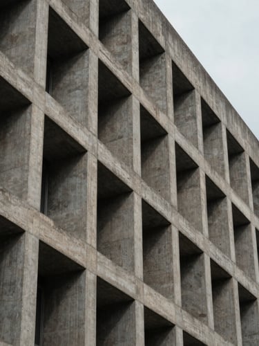 Vertical framing of a brutalist concrete corporate building facade under cool overcast daylight, sharp geometric shadows, emphasizing structural permanence.