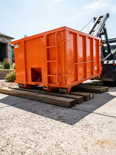 Low-angle sharp industrial photography of a clean safety-orange roll-off dumpster being placed precisely onto protective wooden planks on a concrete driveway, bright midday sun, high-contrast charcoal tones.