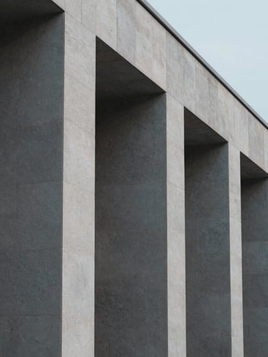 Minimalist architectural detail of a stable modern stone building, shadow lines from clean pillars, soft cool overcast daylight, desaturated tones