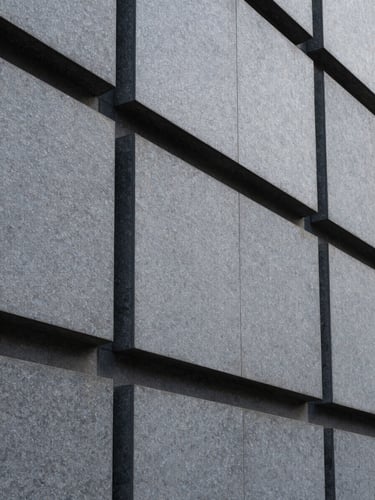 Minimalist architectural detail of a modern corporate building facade, sharp geometric slate-gray stone blocks, clean lines, cool diffused daylight.