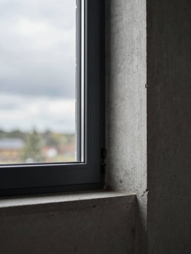 Close-up of modern triple-glazed window joint meeting raw exposed concrete wall, dramatic overcast Baltic light, architectural detail