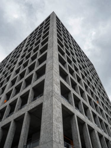 Low-angle architectural photography of a modern concrete and steel skyscraper facade under dramatic overcast daylight, sharp structural shadows, high-contrast cool grays.