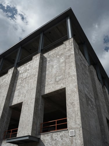 Low-angle architectural shot of concrete and steel building facade under dramatic overcast daylight, casting sharp shadows, high-contrast cool grays.