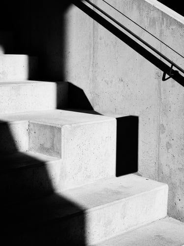 Stark minimalist architectural crop of concrete corporate office stairs, sharp geometric shadows, direct harsh sunlight, high-contrast monochrome, 35mm lens