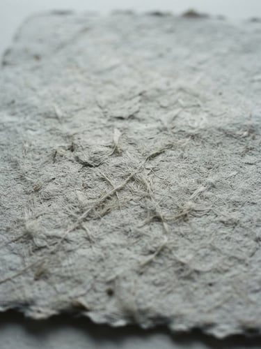 Intimate close-up of textured handmade paper with soft natural shadows, minimalist film photography, desaturated cool tones, high grain, 35mm lens, quiet atmosphere