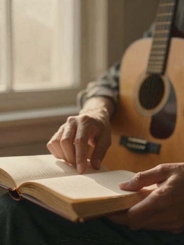 Warm cinematic photography, soft golden-hour window light, muted earthy tones, intimate depth of field, 35mm film grain. Close-up of hands gently turning pages of a worn journal, with an acoustic guitar blurred in the background, framed to the right.