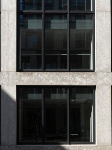 High-contrast architectural shot of a modern concrete and glass facade in London, sharp directional light casting deep diagonal geometric shadows, minimalist crop.