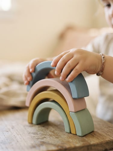 Close-up of a child's hands carefully stacking smooth wooden arches, soft morning light, muted warm cream background, shallow depth of field, 35mm