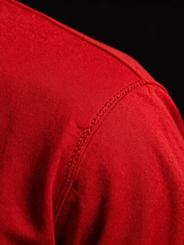 High-contrast macro detail of double-needle stitching on a thick crimson red shoulder seam, sharp studio strobe lighting, deep black background.