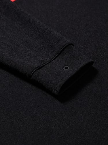 Low-angle close-up of premium heavyweight black cotton fabric texture, showing double-needle stitching on the collar, sharp high-contrast studio lighting with deep shadows.