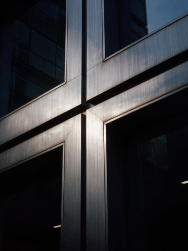 Close-up of brushed metal paneling and dark glass on a premium corporate building, dramatic low-key lighting, high contrast, 35mm