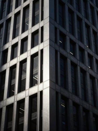 Moody architectural photography of a modern high-end financial district skyscraper corner, low-key dramatic lighting, deep charcoal and brushed silver tones, high contrast, 35mm