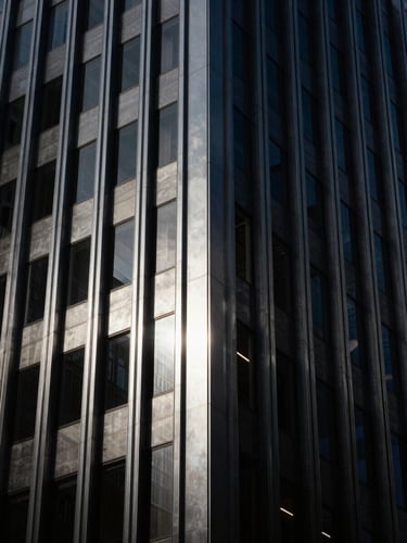 Moody architectural detail of a modern financial skyscraper facade, low-key dramatic lighting with sharp silver reflections, deep charcoal metallic textures, high contrast, 35mm