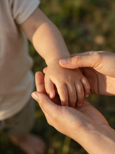 Close-up of hands gently holding a small child's hand, soft natural golden hour light, warm compassionate tones, 35mm photography
