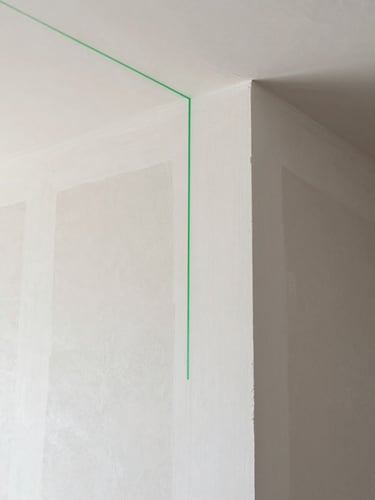 Clean architectural photography, bright natural daylight, crisp plaster textures of a freshly finished drywall corner, a green laser level line casting a precise guide, minimalist composition, 35mm lens