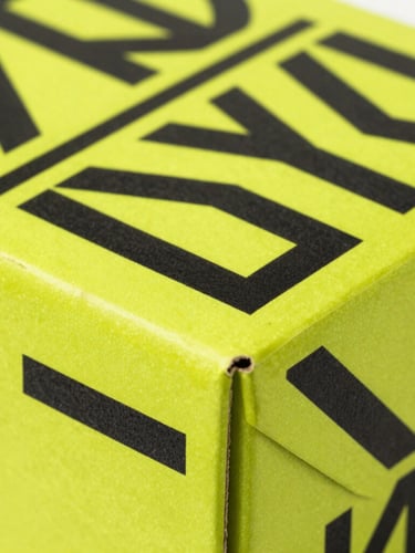 Macro photography of a neon yellow cardboard box with black geometric vector patterns, sharp folded edges, studio lighting, high contrast.
