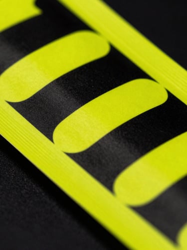 Macro detail of high-contrast printed neon yellow packaging on a matte black background, sharp folds, 35mm photography, dramatic studio lighting