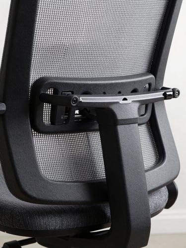 Extreme close-up of an ergonomic chair lumbar mechanism, grey mesh backrest and black polished adjustment lever, overexposed north-facing studio light emphasizing the precision engineering of the sliding lumbar support rail, no human presence