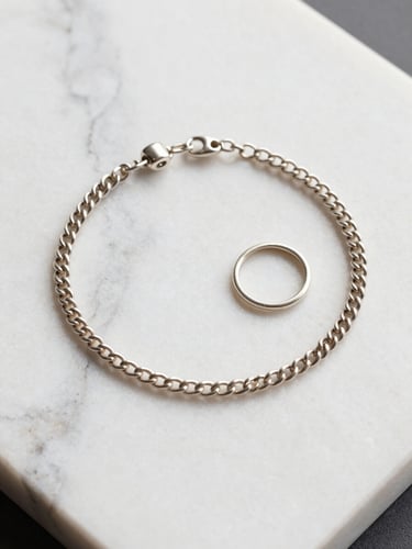 Macro flat-lay of a fine silver anklet and matching toe-ring set arranged on a white marble tile, diffused overhead studio light, the delicate link construction and clasp detail in sharp focus, champagne-silver tones, no hands or model