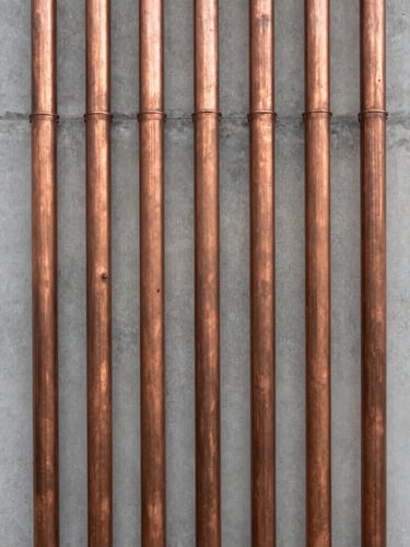 Straight-on architectural shot of perfectly aligned copper conduits running vertically down a minimalist concrete wall, natural side lighting, symmetrical composition.